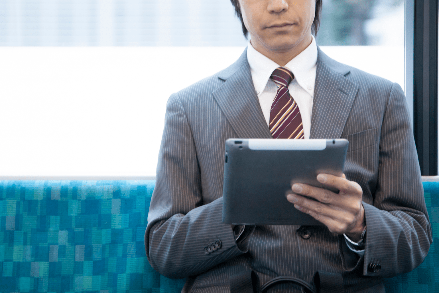 電車内でタブレットを見ているスーツの男性